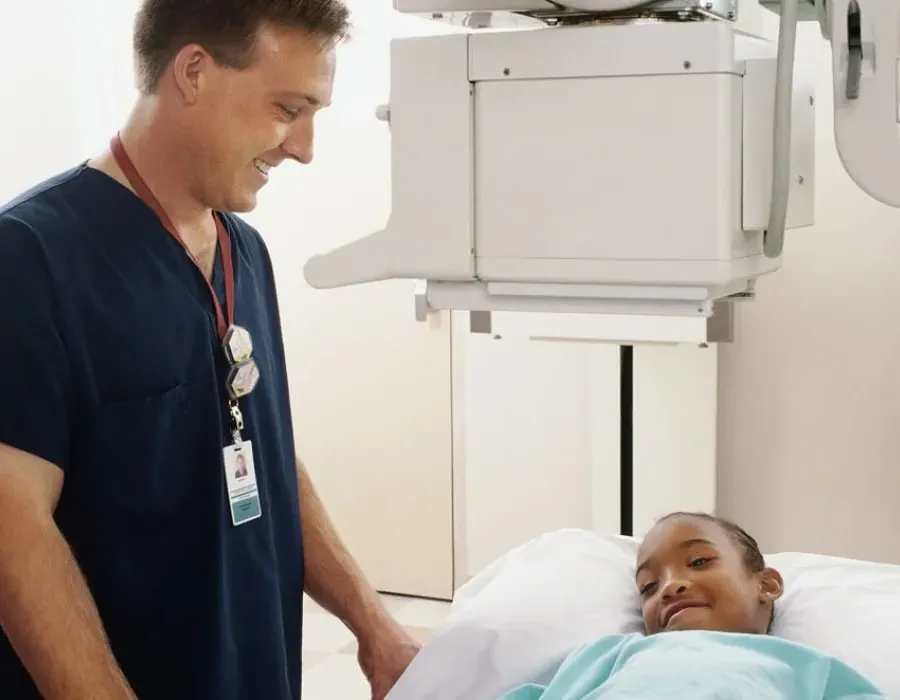 Pediatric nurse speaking with young patient and smiling at bedside in hospital room